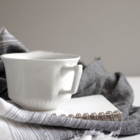 Picture of notebook and white teacup on top of a grey scarf