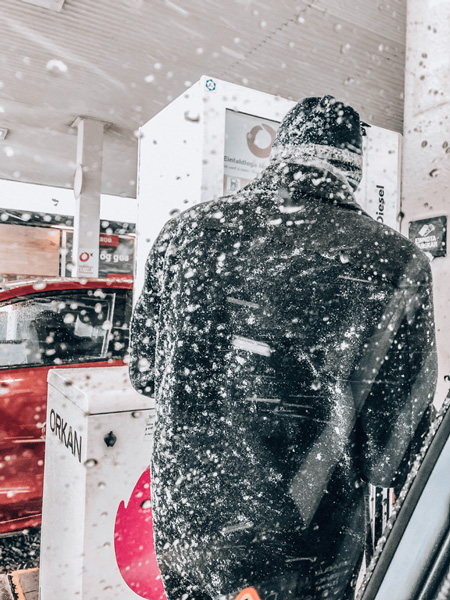 Driving In Iceland In Winter Tip To Keep Gas Tank Full with male wearing black coat and hat covered in show getting gas