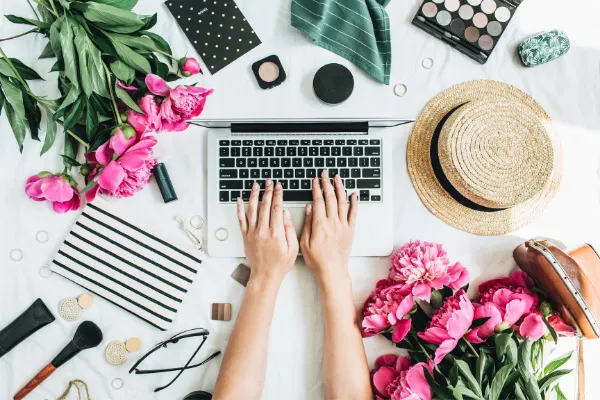 LLC For Bloggers Guide Why & How Register Blog As Business with person typing on laptop, straw hat, pink flowers, glasses