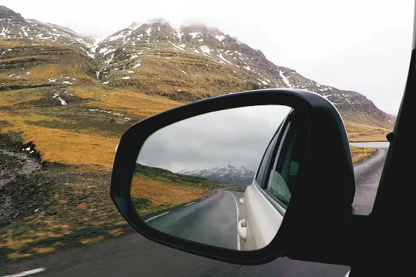 Renting A Car Driving In Iceland In Winter with Icelandic landscape in rearview mirror of car