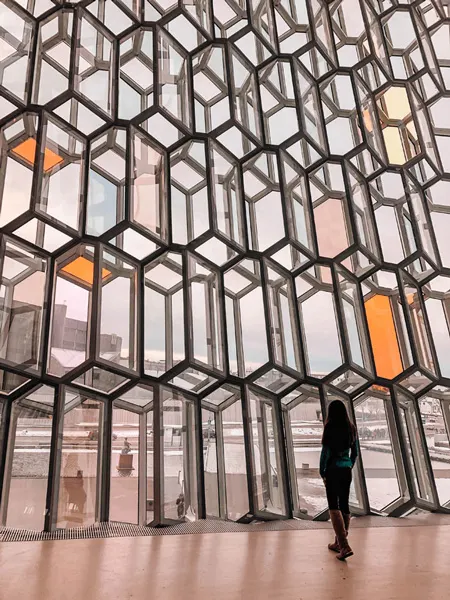 Harpa in Reykjavík Iceland with brunette woman standing in front of geometric stained glasses windows