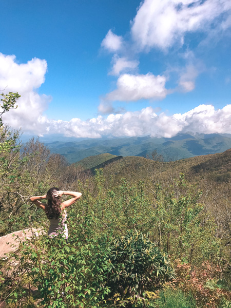 Living In Asheville Pros Hiking with brunette white woman looking out at Blue Ridge Mountains at Craggy Gardens