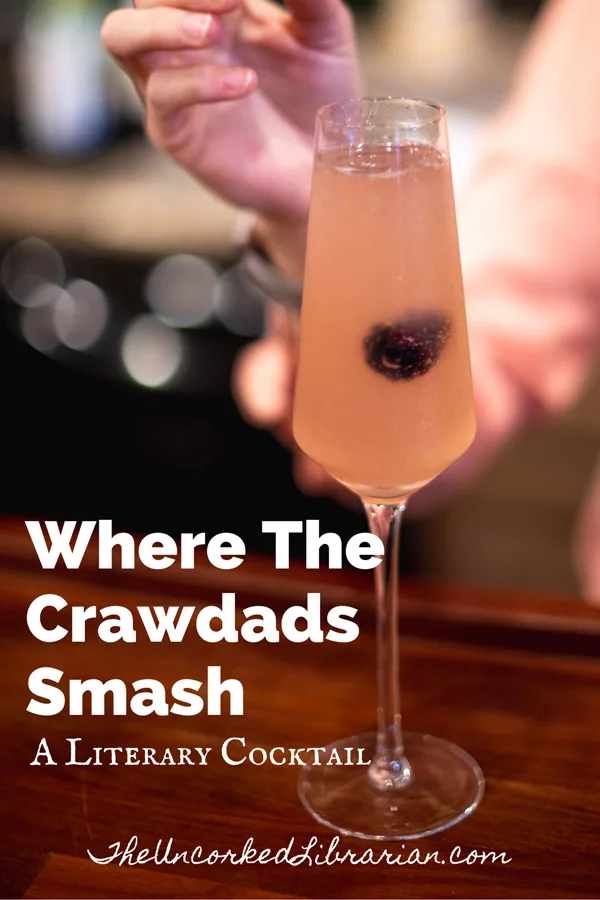 Where The Crawdads Smash Literary Cocktail with champagne flute filled with pink blackberry smash and a woman in a pink blouse dropping in a blackberry