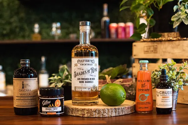 Peach and Gin Cocktail Ingredients, including gin, lime juice, orange syrup, bitters, peach syrup, and vanilla mix