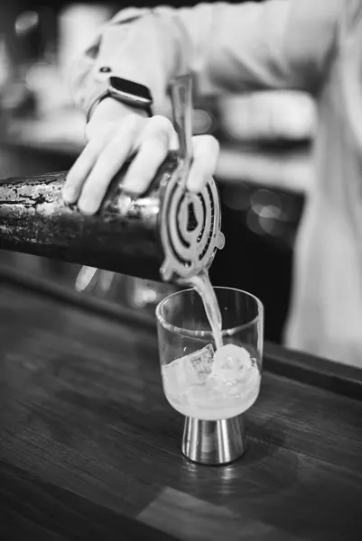 black and white photograph of pouring peach and gin cocktail into a glass