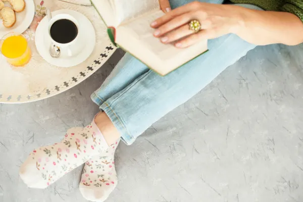 Book blog ideas like how to read more with person sitting on the floor with book and cup of coffee