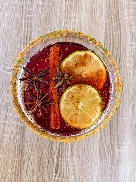 Cheerwine cocktail punch top view of large wine glass filled with red Cheerwine, bourbon, 2 lime slices, 3 anise stars, and a cinnamon stick