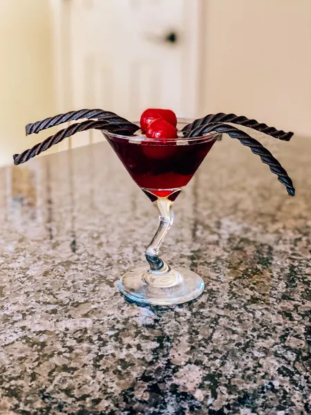 Black Widow Mead Martini with red cocktail in martini glass with cherries and licorice in shape of black widow spider