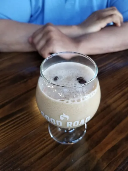 Coffee Mead Cocktail with glass filled with coffee drink and floating coffee beans with person in blue shirt's arms in the background 