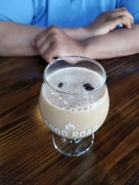 Coffee Mead Cocktail with glass filled with coffee drink and floating coffee beans with person in blue shirt's arms in the background