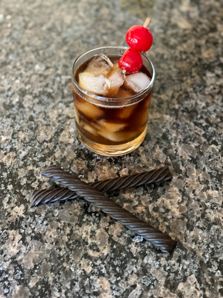 Rum and Coke Mead Cocktail Recipe with 2 black licorice sticks and rum and coke in lowball rocks glass with ice and cherry garnish