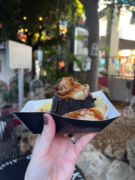 Drunk's Denial Food Truck in Aruba with white hand and painted nails holding up chocolate cake covered with whiskey infused pears in front of outdoor shopping area