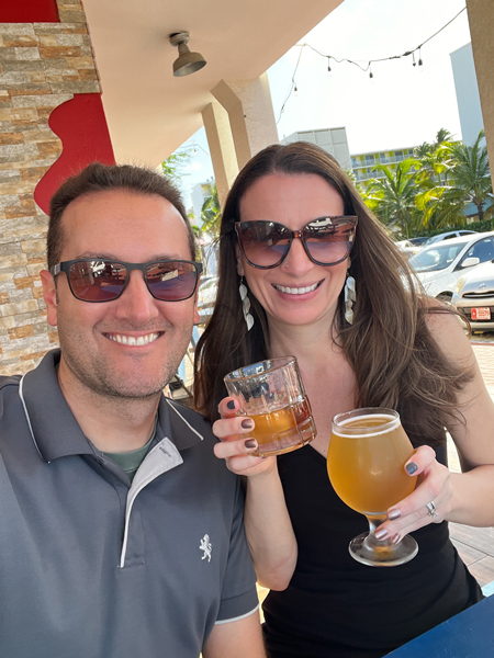 Fireson Brewery in Aruba with white brunette male and female wearing sunglasses holding a cocktail and blonde craft beer