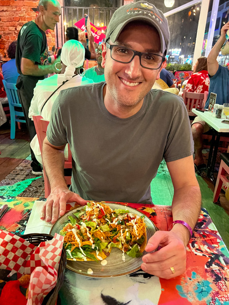 Kalin's Mexican Cuisine Restaurant in Aruba with white brunette male in green shirt with glasses and baseball hat eating gluten-free tostados at a colorful table