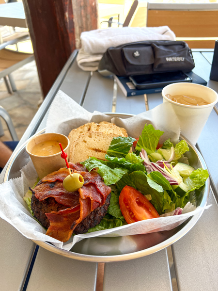 Oceanside Bar & Grill in Aruba burger on gluten-free bun with bacon and green olive on toothpick with side salad with lettuce and tomatoes