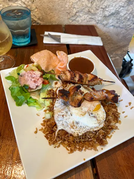 Bistro de Suikertuin Restaurant in Aruba Nasi Goreng, which is Indonesian fried rice, on white plate topped with egg and paired with peanut sauce with chicken skewers