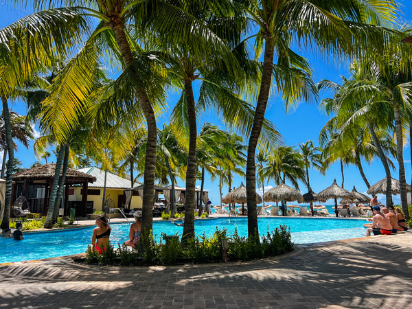 Holiday Inn Resort in Aruba Pool with palm trees, people sitting with legs in water, and Palm Beach in the background