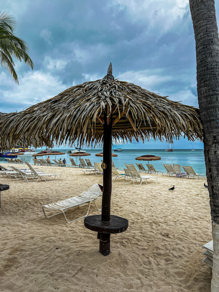 Palm Beach in Aruba Shelter with umbrella-leaf like top, table and white chairs with brown sand and bright blue water