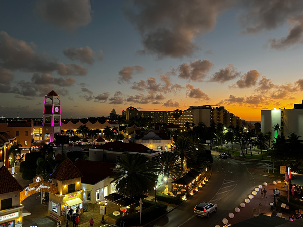 Paseo Herencia Mall at night from above with lit up clock tower, sunset over Palm Beach, and clouds in the sky