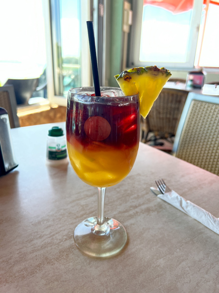Rum Reef on Baby Beach Aruba Restaurant with red and orange sangria garnished with a pineapple on table with windows overlooking the beach in the background