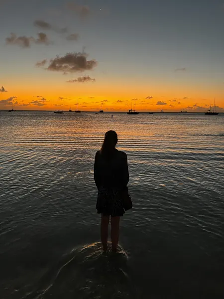 Sunset at Palm Beach in Aruba with woman with back to camera watching the orange sun set over water