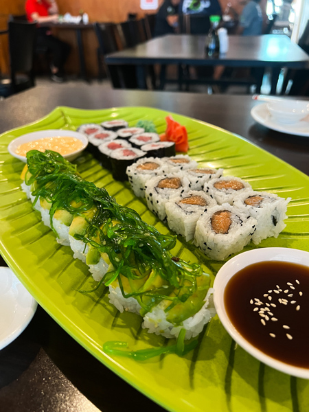 Yami Yami Aruba restaurant with sushi rolls on green plate in the shape of a leaf with spicy mayo and a brown sauce in small bowls