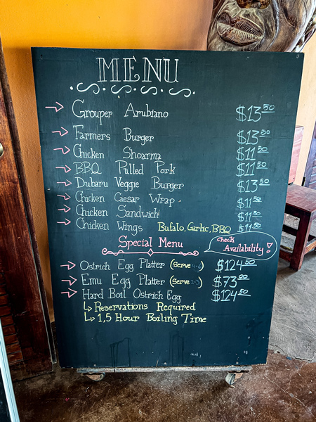 Aruba Ostrich Farm's Savana Bar and Restaurant menu on black chalkboard with food written out with prices like a burger, pulled pork, and ostrich egg