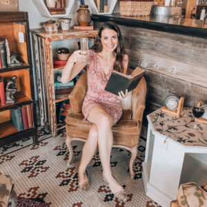 Christine Owner The Uncorked Librarian LLC with white brunette female in pink dress sitting in chair with glass of white wine and open book